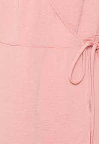 Pehmee roosa kangas, millel on veidi tekstuuriga viimistlus, pakub mähkides disaini ja vöö kohal reguleeritavuse jaoks sidumisdetaili.