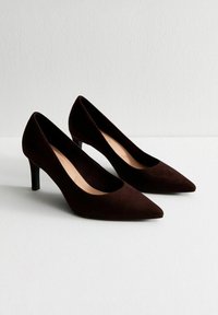 Scarpe con tacco alto in suede marrone, dal design a punta e dalla silhouette classica, caratterizzate da un tacco sottile e una fodera interna liscia.