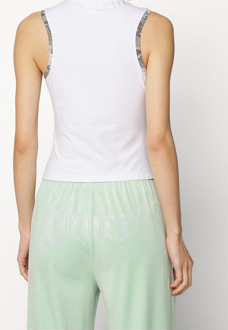 Bílý top bez rukávů se stříbrnými akcenty, kombinovaný s mentolově zelenými kalhotami, na kterých je na zadní straně „Juicy“ posetý rhinestones. Jemná textura materiálu.