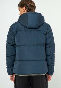 Marine pufferjack met capuchon, voorzien van geborduurd stiksel, een gladde textuur en elastische manchetten. Ontwikkeld voor warmte en comfort.