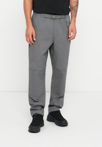 Gray cargo pants with a flexible waistband, multiple pockets, and articulated knee panels for movement; paired with black, sturdy footwear.