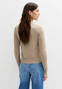 Stickad beige tröja med långa ärmar, ribbad mudd och fåll, med en klassisk skärning. I kombination med ljusblå vida jeans.