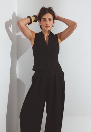 Black sleeveless top with a collar and front button closure, paired with wide-leg black pants featuring pleats. Smooth fabric texture.