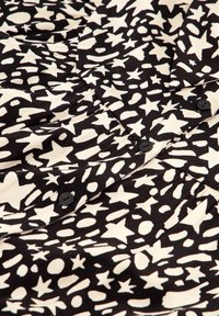 Black and cream patterned fabric featuring various star and shape motifs with button details, showcasing a soft, textured surface.