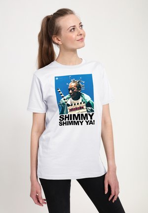 T-shirt blanc avec un imprimé graphique d'une personne avec des tresses tenant une clapperboard, avec un texte noir disant "SHIMMY SHIMMY YA !"