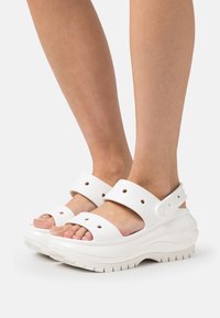 Sandalias de plataforma blancas con suela texturizada, dos correas anchas con recortes circulares y una corredera en el talón ajustable.