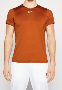 Orange Nike träningströja tillverkad av ett lätt material, med v-ringning och korta ärmar, och med en liten vit logotyp på bröstet.