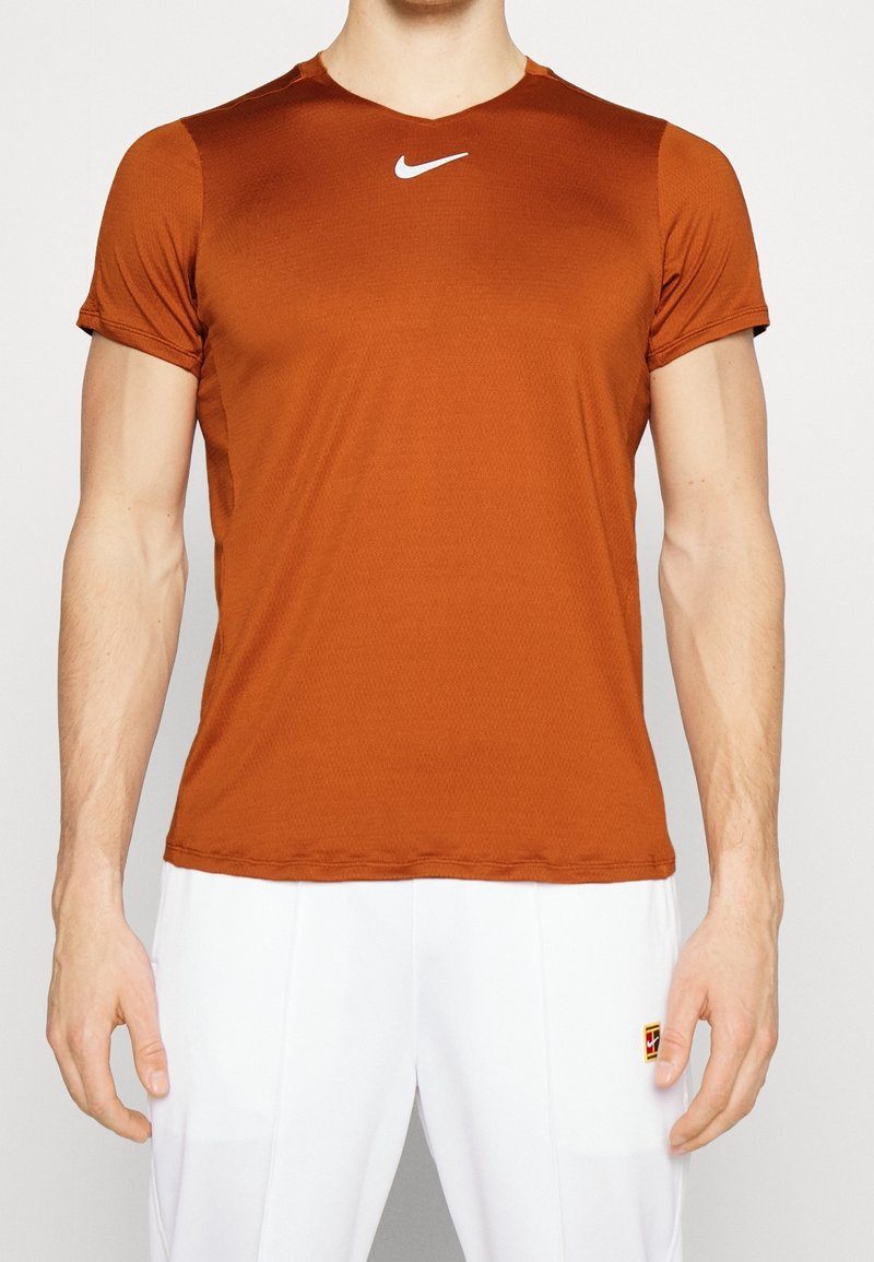 Orange Nike träningströja tillverkad av ett lätt material, med v-ringning och korta ärmar, och med en liten vit logotyp på bröstet.