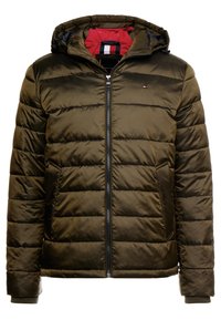 Khaki péřová bunda s kapucí, prošívaným designem, kontrastní červenou podšívkou, zapínáním na zip a bočními kapsami. Modelka má na sobě volný střih.