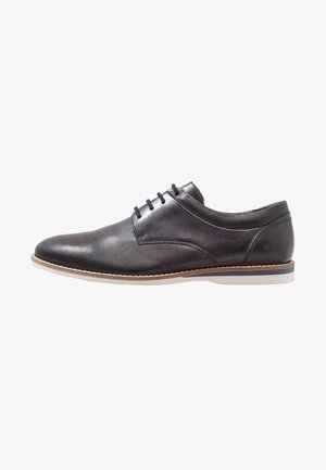 Zapato de vestir de cuero gris oscuro con un acabado suave y texturizado, que presenta seis ojales, una suela blanca de perfil bajo y detalles de costura.