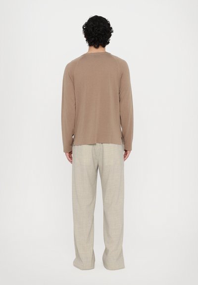Brown long-sleeve top with a straight cut and crew neck, paired with light beige, loose-fitting trousers featuring a textured pattern.
