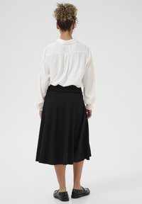 Jupe midi noire avec un design évasé et une taille élastique, associée à un chemisier blanc au fit décontracté et aux manches retroussées.