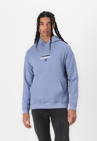 Light blue hoodie with a front pocket and ribbed cuffs. Features graphic text in white and black on the chest. Soft cotton material.