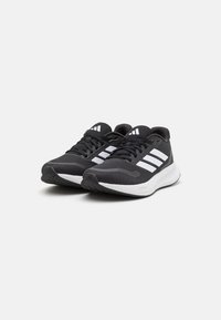 Černé sportovní boty z síťoviny a syntetických materiálů. Mají tři bílé pruhy, texturovanou podrážku a polstrovanou bílou mezipodešev.