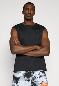 Haut de sport sans manches noir avec un col rond et un petit logo sur la poitrine, associé à un short à motifs en noir et blanc.