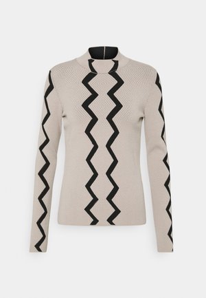 Pull en maille beige à manches longues avec des motifs zébrés noirs au centre devant et le long des manches, avec un col rond montant.