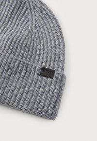 Grå strikket lue med vertikal ribbing, med et lite svart lærmerke som har ordet "BOSS." Myk tekstur og brettet oppbrett.
