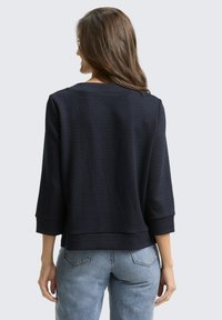 Marineblauw gestructureerd top met driekwart mouwen en een brede halslijn, voorzien van een effen patroon en een relaxte pasvorm. Draagt met lichtblauwe jeans.
