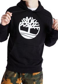 Sudadera negra con un gran logo blanco de un árbol en el pecho, con un bolsillo tipo canguro y cordones ajustables en la capucha.