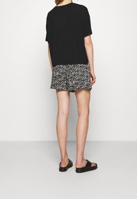 Zwart oversized T-shirt met korte mouwen, gecombineerd met zwart-witte korte broek met luipaardprint. Lichtgewicht stof. Zwarte instapsandalen.