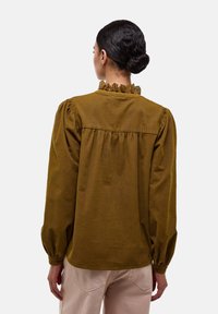 Blouse en vert olive, texturée, avec un col froncé et des manches ballon, présentant une coupe ample et un empiècement froncé. Convient pour un style décontracté.