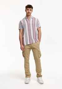 Camisa de manga corta a rayas en rojo, azul y blanco con botones, combinada con pantalones cargo beige que cuentan con bolsillos laterales y un corte relajado.