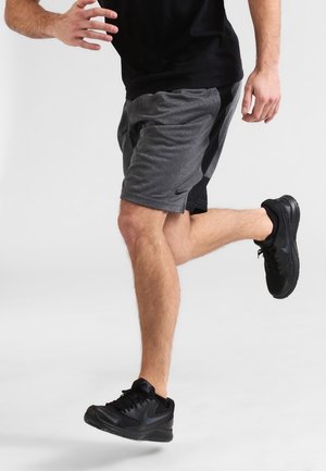 Szare spodenki sportowe z czarnymi panelami bocznymi, noszone z czarną koszulą i czarnymi butami sportowymi, z logo Nike na spodenkach.