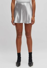 Zilveren satijnen minirok met een flared ontwerp, gladde textuur en een tailleband. Draagt deze met zwarte kniehoge sokken en puntige schoenen.