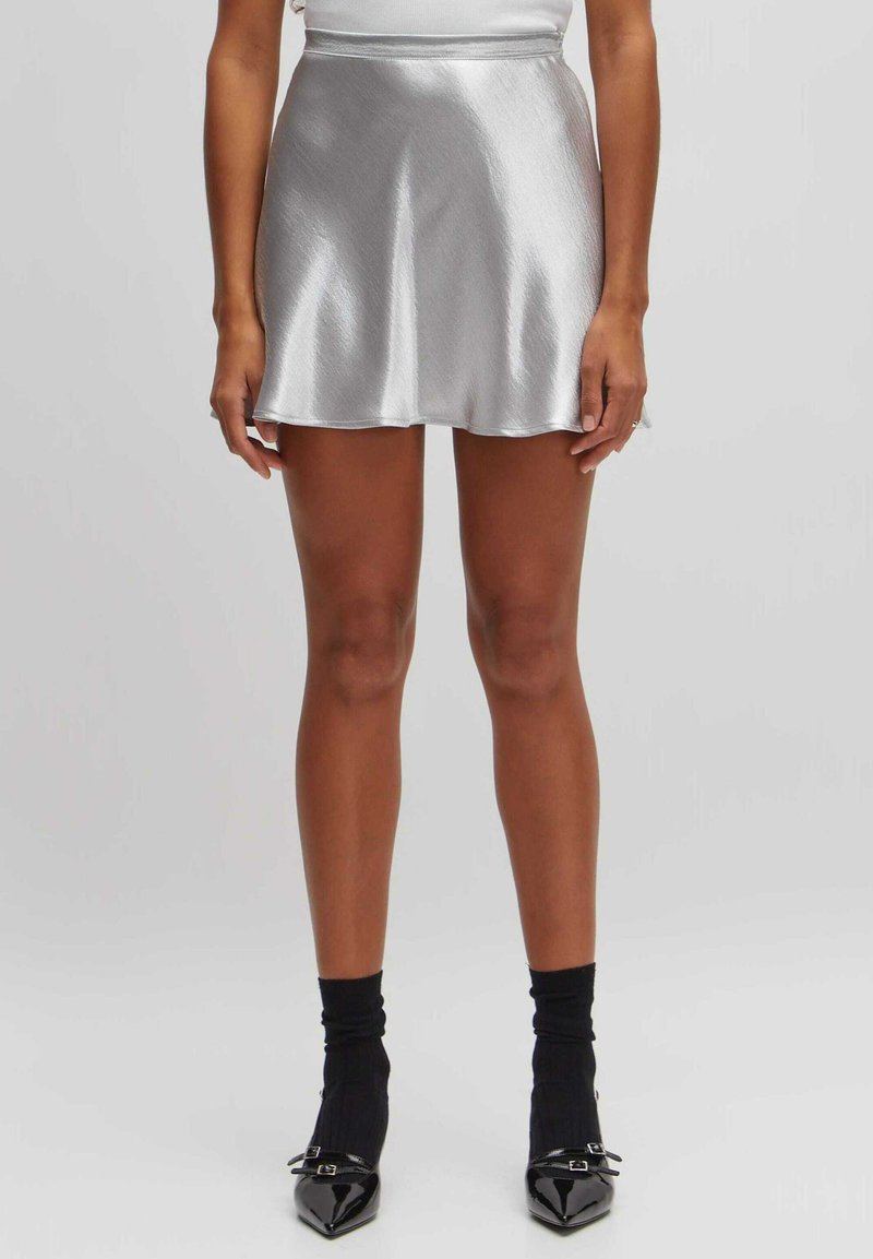 Zilveren satijnen minirok met een flared ontwerp, gladde textuur en een tailleband. Draagt deze met zwarte kniehoge sokken en puntige schoenen.