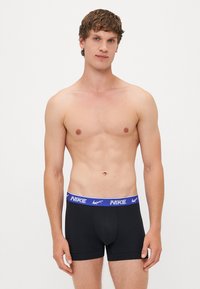 Fekete boxer nadrág sima anyagból, kék és fehér derékrésszel, rajta a "NIKE" márkajelzéssel. Klasszikus fazon, támogató kialakítással.