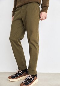 Pantalons vert olive avec une coupe décontractée, dotés de poches latérales et d'une texture douce. Assortis à des baskets noires et marron avec des lacets.