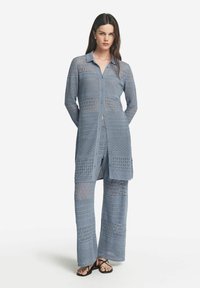 Ljust blått virkade outfit bestående av en lång skjorta med knappringning och matchande vida byxor, båda med strukturerade mönster och semi-transparent design.