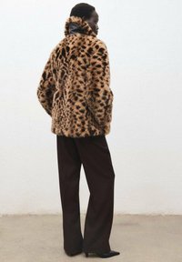Giacca in pelliccia sintetica con stampa leopardata, colletto alto e spalle scese, abbinata a pantaloni neri a vita alta e scarpe nere a punta.