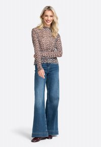 Long-sleeve, sheer top in light beige with a black leopard print, paired with wide-leg blue jeans and dark red shoes.