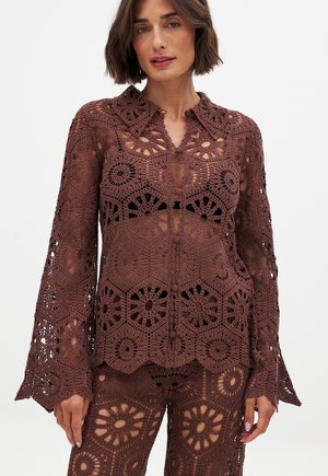 Blusa in cotone all'uncinetto marrone con intricati motivi floreali e geometrici, colletto e maniche lunghe a campana con dettagli aperti.