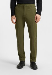 Olivegröna byxor med skräddarsydd passform, tillverkade av ett mjukt tyg. Har knappstängning och en ren, rak ben-design. Svarta skor bärs.