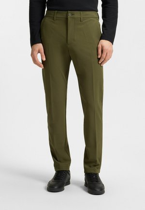 Olijfgroene broek met een op maat gemaakte pasvorm, gemaakt van een gladde stof. Kenmerkt zich door een knoopsluiting en een strakke, rechte pijpdesign. Zwarte schoenen gedragen.