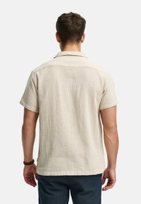 Kortærmet, beige, struktureret skjorte med kravehalsudskæring, der har en afslappet pasform og en lige kant, båret med marineblå bukser.