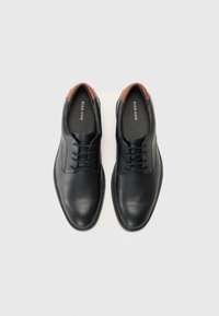 Chaussures noires en cuir avec une finition lisse, présentant un accent marron au talon, un design à lacets et un bout rond.