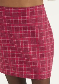 Röd rutigt kjol med en strukturerad tyg, som har ett litet vitt rutig mönster, och en rak skärning vid fållen.