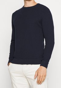 Pull en tricot bleu marine avec un motif texturé, col rond, et poignets et ourlet côtelés. Coupe décontractée adaptée au superposition.