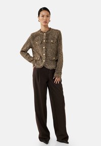 Bruine tweedjas met een gestructureerde afwerking, met een ronde halslijn, knopen en twee broekzakken. Gecombineerd met een donkere broek.