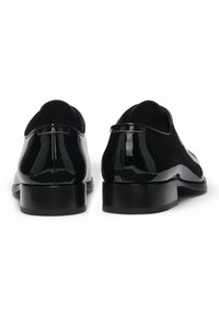 Een paar zwarte glanzende leren formele schoenen gezien vanaf de achterkant op een witte achtergrond.