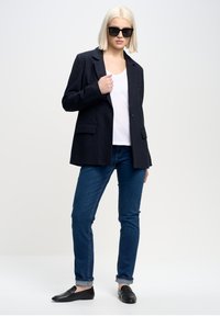 Mörkt randigt blazer med slag, vit t-shirt, blå slim-fit jeans och svarta loafers. Har rak passform och minimalistisk design.