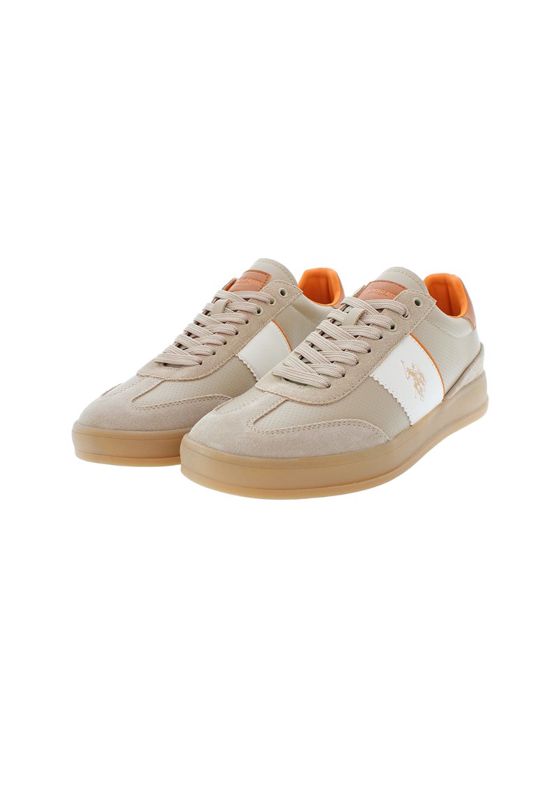 Zapatillas beige con parte superior de ante y malla, panel lateral blanco, acentos naranjas en la lengüeta y el talón, y una suela de goma translúcida.
