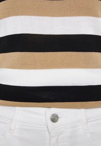 Strik toppen med vandrette beige, hvide og sorte striber, stoppet ned i hvid højhalsede jeans med en synlig sølvknap.
