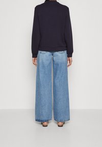 Navy sweatshirt with ribbed hem, paired with wide-leg light blue denim jeans featuring a faded wash and frayed hem.
