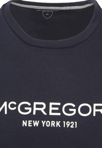 Donker marineblauwe t-shirt met een ronde halslijn, gemaakt van zachte katoen. Kenmerkt zich door vetgedrukte witte tekst: "McGREGOR NEW YORK 1921" die opvallend wordt weergegeven.