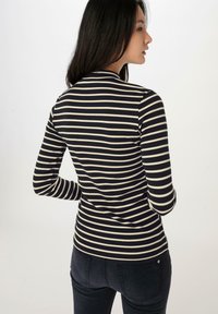 Langsleeve gestreepte top in marineblauw en crème, met ribbelstructuur, aansluitend design, hoge halslijn en contrasterende kleuren. Zicht van de achterkant.