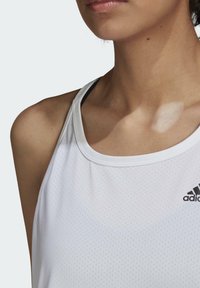 Vitt atletiskt linne med ventilerande mesh-tyg, utrustad med klassisk rund halsringning och svart Adidas-logotyp på vänster bröst.